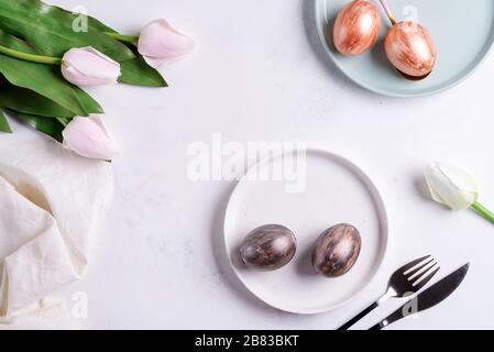 Greeting Easter card with handmade painted bright eggs on a plates and tulips flowers on a light grey marble background. Stock Photo