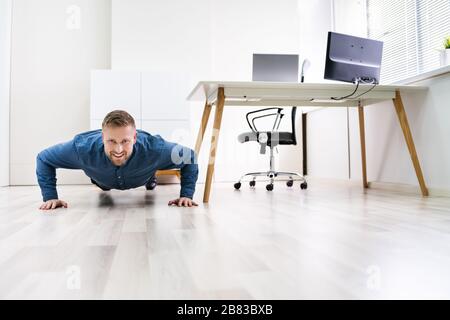 Businessman Doing Push Up On Hardwood Floor In Office Stock Photo