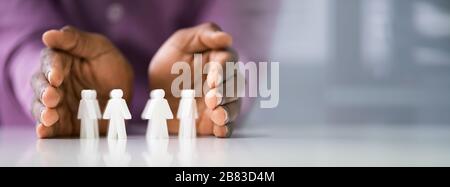 Close-up Of A Human Hand Protecting Red Human Figures On White Background Stock Photo