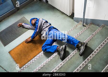 Unconscious Handyman Lying On Staircase With Helmet On Floor Stock Photo