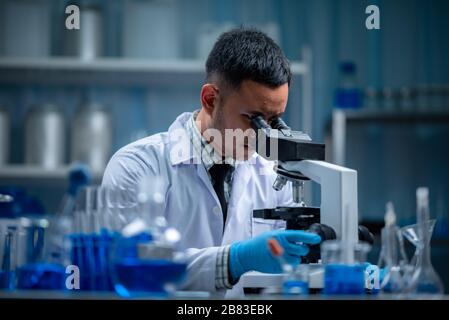 Young scientist looking through a microscope in a laboratory. Young scientist doing some research. Stock Photo