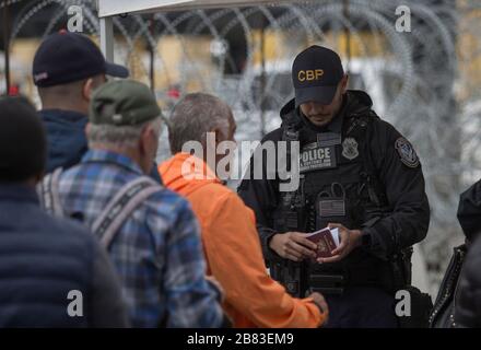 Tijuana, Mexico. 18th Mar, 2020. A border official checks a passport at the border crossing between Tijuana and the USA. Despite the threat of possible restrictions on entry regulations by the USA, people are allowed to cross the border without special measures. Mexico has so far reported 118 Covid-19 infected persons. USA has almost 10 000 confirmed cases. Credit: Omar Martínez/dpa/Alamy Live News Stock Photo