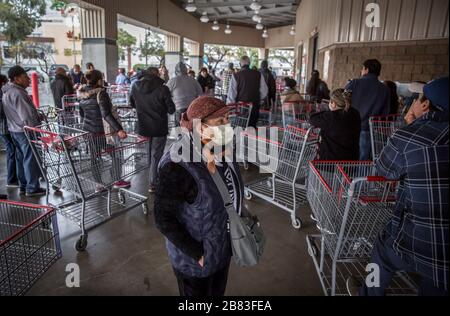 Tijuana, Mexico. 18th Mar, 2020. A woman with a face mask stands between shopping trolleys, while numerous people queue up in front of a wholesaler. Fearing the spread of the coronavirus, people queue up early in front of the supermarket. Mexico has so far reported 118 Covid-19 infected people. The US has almost 10,000 confirmed cases. Credit: Omar Martínez/dpa/Alamy Live News Stock Photo