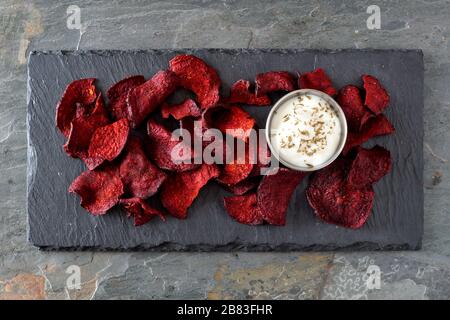 Healthy beet chips with dip, above view on a stone server and slate background Stock Photo