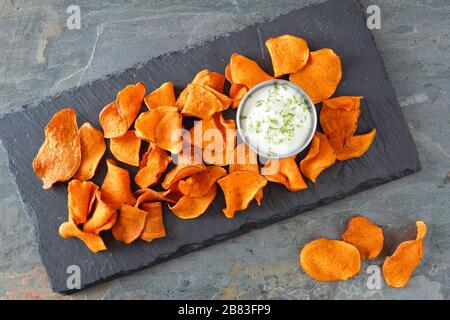 Healthy vegetable chips with dip, above view on a stone server and slate background Stock Photo