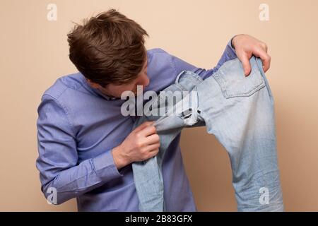Hole and threads on denim jeans. Sad caucasian man holding destroyed blue jeans showing holes. Stock Photo