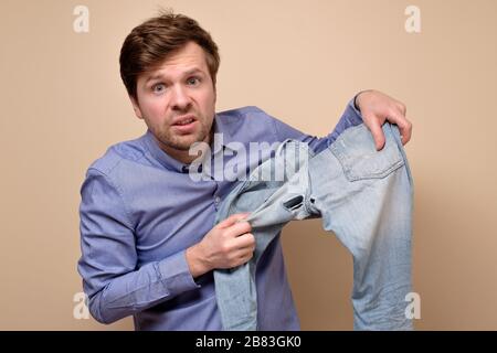 Hole and threads on denim jeans. Sad caucasian man holding destroyed blue jeans showing holes. Stock Photo