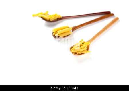 Various types of italian pasta concept. Raw gemelli, penne, casarecce in wooden spoons on white background. Copy space. Stock Photo