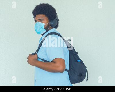A man in a blue shirt using black headphones, a backpack and wearing a medical mask to avoid contagion Stock Photo