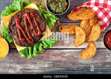 Picnic scene with barbecued hamburger and potato wedges over dark rustic wood Stock Photo