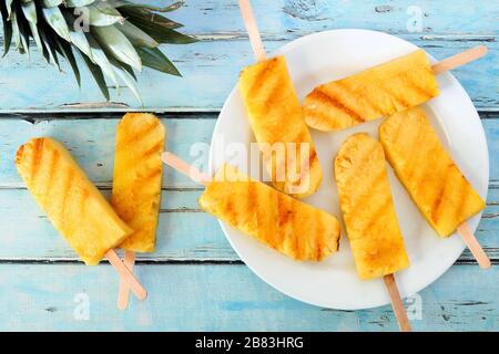Plate of sweet grilled summer pineapple wedges against a rustic blue wood background Stock Photo
