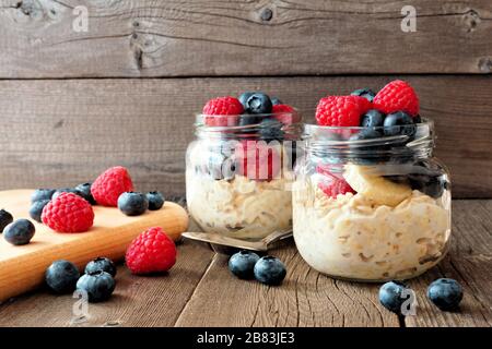 Overnight oats with fresh blueberries and raspberries in jars on a rustic wood background Stock Photo