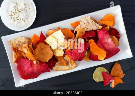 Plate of colorful healthy vegetable chips with dip, above view on a slate background Stock Photo