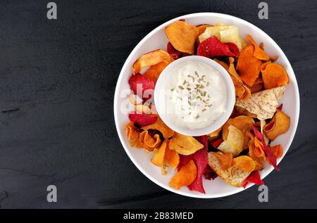 Plate of colorful organic vegetable chips with dip overhead view on a slate background Stock Photo