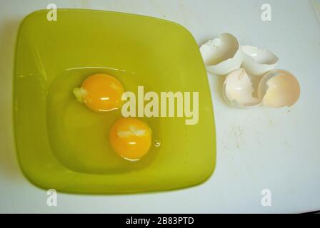 Close up of two raw eggs in a green plastic bowl and eggshells Stock Photo