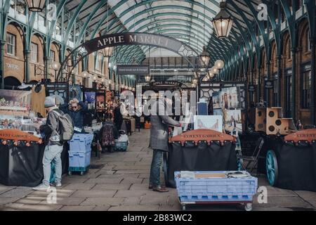 London, UK - March 06, 2020: Sellers and customers by the stalls in Apple Market inside Covent Garden, one of the most popular tourist sites in London Stock Photo