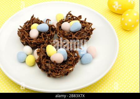 Plate of springtime chocolate nests filled with Easter eggs on a yellow background Stock Photo