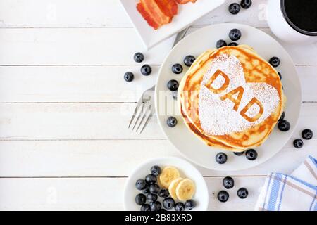 Pancakes with heart shape and DAD letters. Fathers Day breakfast concept. Top view side border on a white wood background. Stock Photo