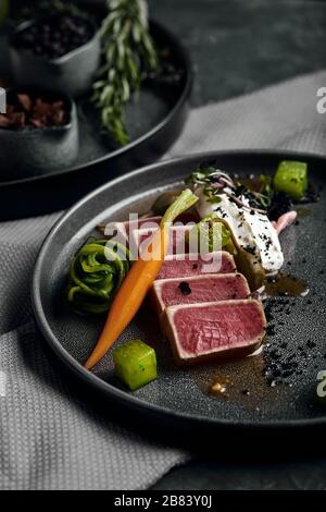 Tuna tagliata in vegetables stewed carrots and peppers, Beautiful serving, traditional Italian cuisine, gray background, copy space. food concept. Stock Photo