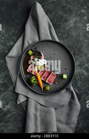 Tuna tagliata in vegetables stewed carrots and peppers, Beautiful serving, traditional Italian cuisine, gray background, copy space. food concept. Stock Photo