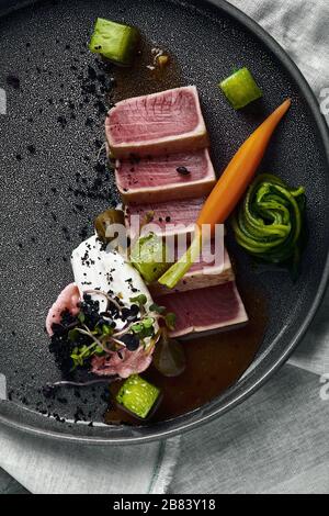 Tuna tagliata in vegetables stewed carrots and peppers, Beautiful serving, traditional Italian cuisine, gray background, copy space. food concept. Stock Photo