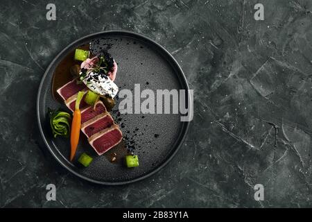 Tuna tagliata in vegetables stewed carrots and peppers, Beautiful serving, traditional Italian cuisine, gray background, copy space. food concept. Stock Photo