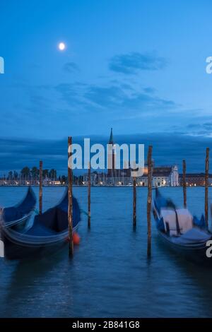 Bright moon above San Giorgio Maggiore island and church.  Gondolas floating on moving water are blurred by long exposure.  Venice, Italy Stock Photo