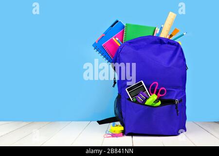 Purple backpack full of school supplies against a blue background. Back to school concept. Copy space. Stock Photo