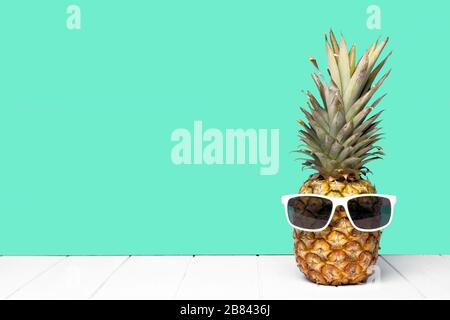 Hipster pineapple with sunglasses against a teal colored background. Minimal summer concept. Stock Photo