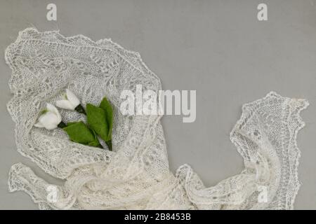 Two snowdrops made of wool in the lower left corner wrapped in a down knitted shawl on a grey plaster background. Stock Photo