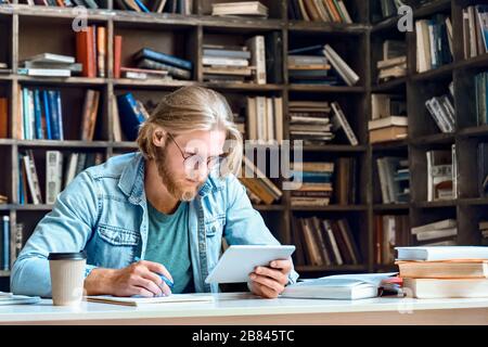 Focused man student using digital tablet make notes study online in library. Stock Photo