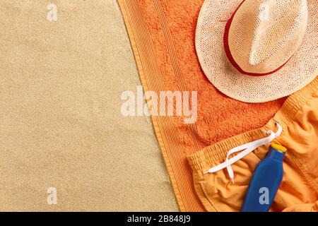 Top view of sandy beach with summer accessories. Background with copy space and visible sand texture. Border composition made of towel. Stock Photo