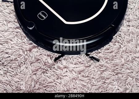 Automatic robot vacuum cleaner in black on a gray shag carpet. New modern technologies for apartment cleaning. smart home electronic assistant Stock Photo