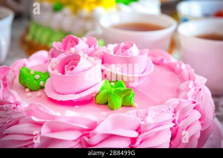 beautiful pink cream cake on the background of tea mugs. Evening tea with sweets. Roses and cream on the cake. Stock Photo