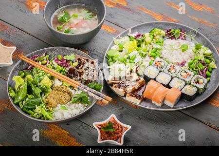 Close up pan-Asian dishes in bowls. Rice with spices and beef, salad with beans, rolls with salmon and avocado, fish soup. Tasty and healthy nutrition Stock Photo