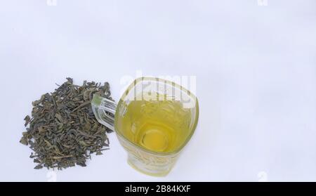Green tea in a cup with heap of dried green tea leaves isolated on white background.Upper view. Stock Photo