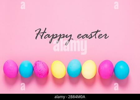 Colored eggs lie in a row on a pink background text Happy Easter. Festive spring concept. Copy space flat lay banner Stock Photo