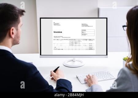 Close-up Of Two Businesspeople Analyzing Invoice On Computer Stock Photo