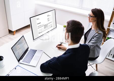 Close-up Of Two Businesspeople Analyzing Invoice On Computer Stock Photo