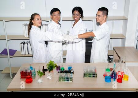 Professional young chemists in white coats shaking hands in scientific laboratory. Stock Photo