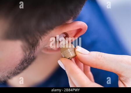 Doctor Inserting Hearing Aid In Man's Ear In Clinic Stock Photo