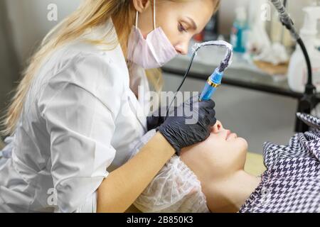 Microblading eyebrows work flow in a beauty salon. Woman having her eye brows tinted. Semi-permanent makeup for eyebrows. Focus on model's face and ey Stock Photo