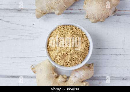 Grounded ginger and ginger root on white wooden surface. Stock Photo