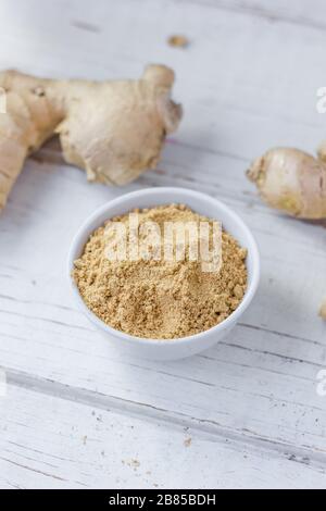 Grounded ginger and ginger root on white wooden surface. Stock Photo