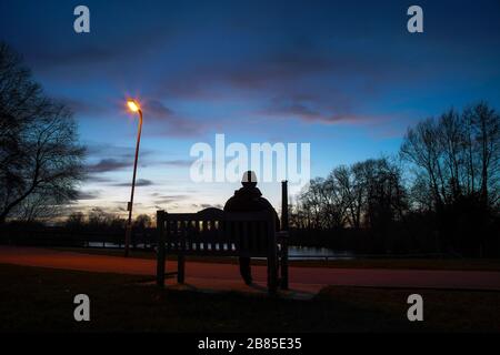 Isolated man on park bench, UK, at dusk, twilight Stock Photo