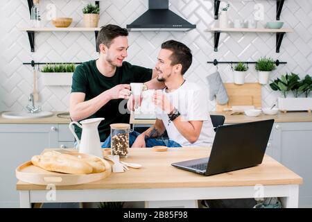 Happy gay couple drinking coffee and having fun together. Everyday morning routine of gay couple life in kitchen at home. Gay concept, happy life. Stock Photo