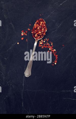 Spoon full of chilli flakes on black marble from above Stock Photo