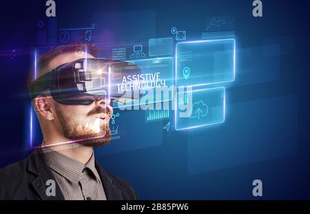 Businessman looking through Virtual Reality glasses with ASSISTIVE TECHNOLOGY inscription, new technology concept Stock Photo