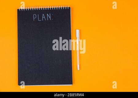 Wide view image of blank black spiral note pad and white marker with calligraphic inscription plan on yellow background Stock Photo