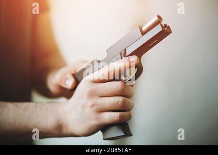 The man is holding a black airsoft gun, illuminated by light, and reloading it. Stock Photo